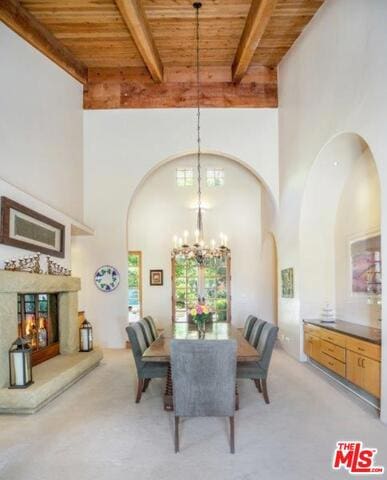 carpeted dining room featuring wood ceiling, a towering ceiling, and beamed ceiling