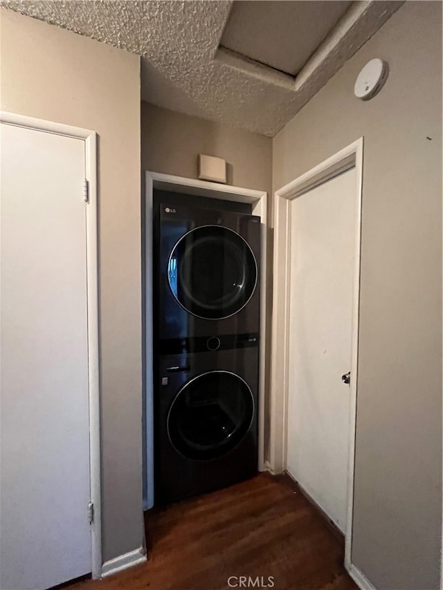 laundry room with a textured ceiling, stacked washer / dryer, and dark wood-type flooring