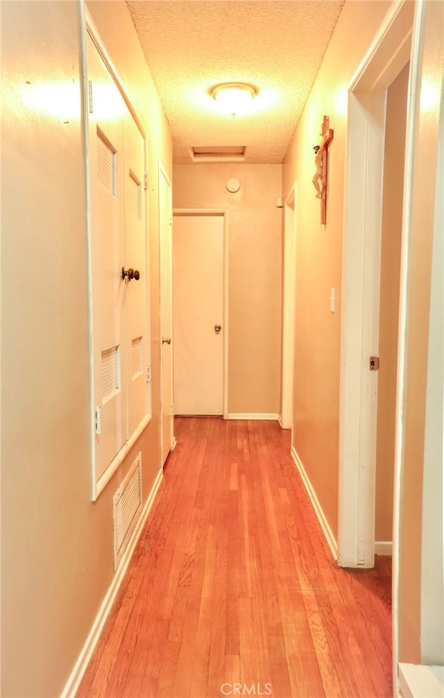 hall with light wood-type flooring and a textured ceiling