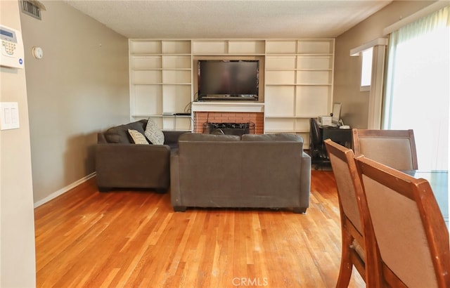 living room featuring a brick fireplace, a textured ceiling, and light hardwood / wood-style flooring