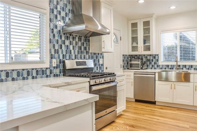 kitchen featuring appliances with stainless steel finishes, white cabinetry, wall chimney range hood, and a wealth of natural light