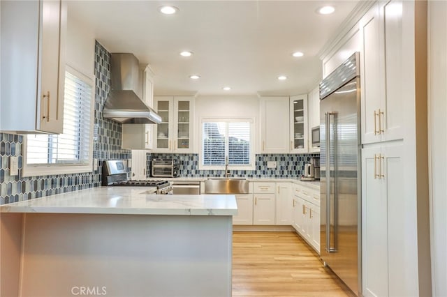 kitchen featuring white cabinets, kitchen peninsula, wall chimney exhaust hood, stainless steel appliances, and light hardwood / wood-style floors