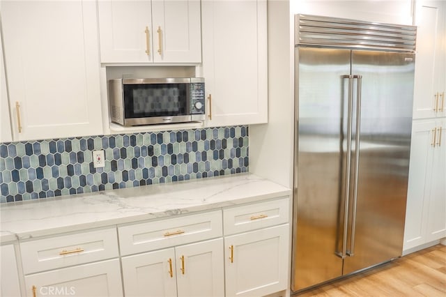 kitchen featuring light stone counters, light hardwood / wood-style floors, white cabinetry, decorative backsplash, and appliances with stainless steel finishes