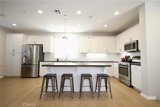 kitchen with appliances with stainless steel finishes, hanging light fixtures, light wood-type flooring, and white cabinets