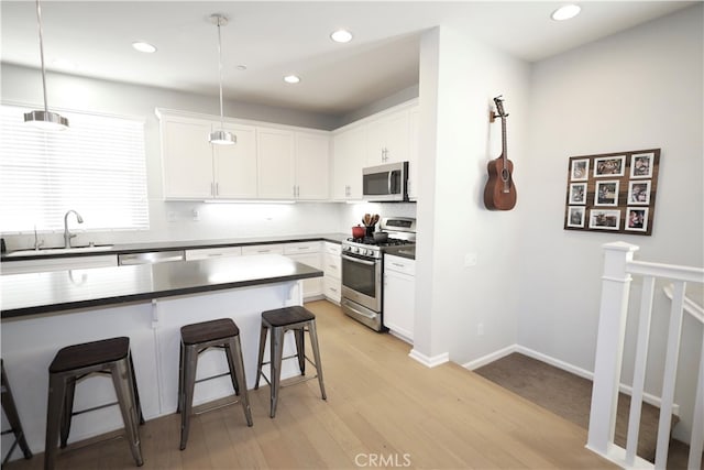 kitchen with a breakfast bar, white cabinets, appliances with stainless steel finishes, and hanging light fixtures