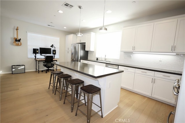 kitchen with a breakfast bar area, white cabinets, hanging light fixtures, light hardwood / wood-style flooring, and stainless steel appliances