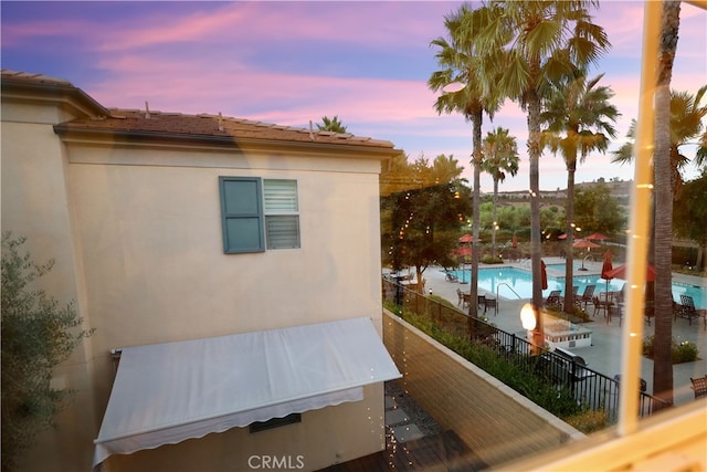 property exterior at dusk with a balcony and a community pool