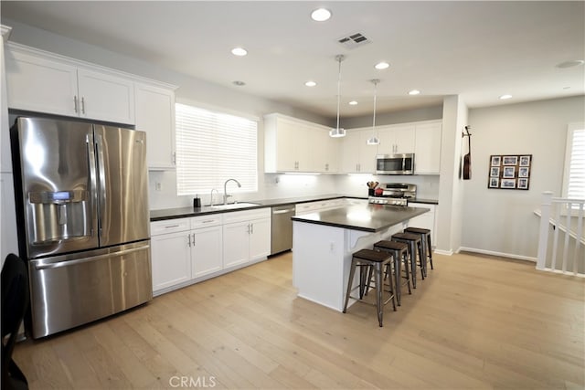 kitchen featuring appliances with stainless steel finishes, hanging light fixtures, a kitchen island, light wood-type flooring, and sink