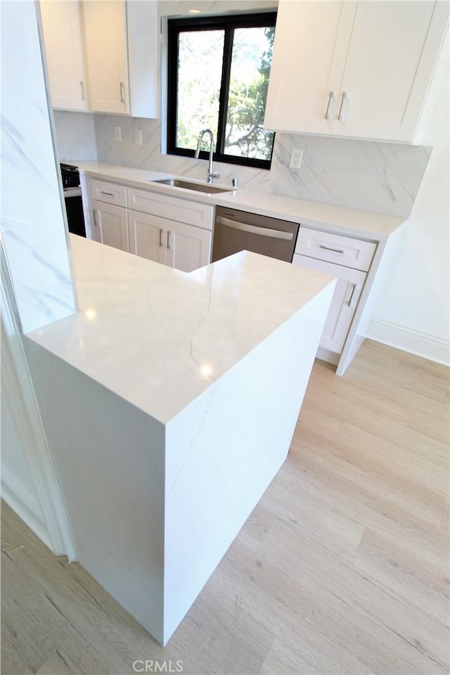 kitchen with light wood-type flooring, tasteful backsplash, sink, dishwasher, and white cabinetry