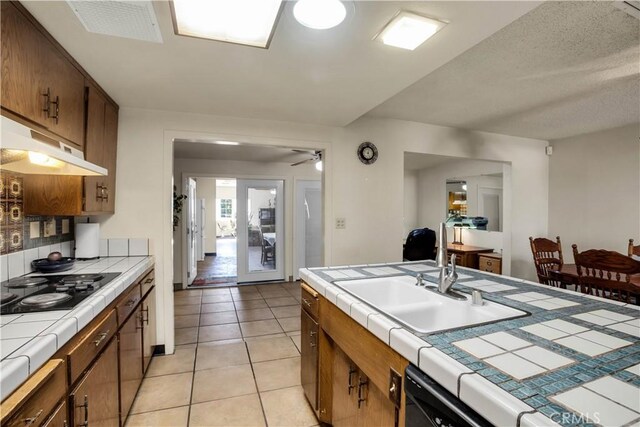 kitchen featuring ceiling fan, light tile patterned flooring, sink, stainless steel dishwasher, and tile counters