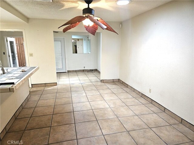 unfurnished living room featuring ceiling fan, a textured ceiling, and light tile patterned floors