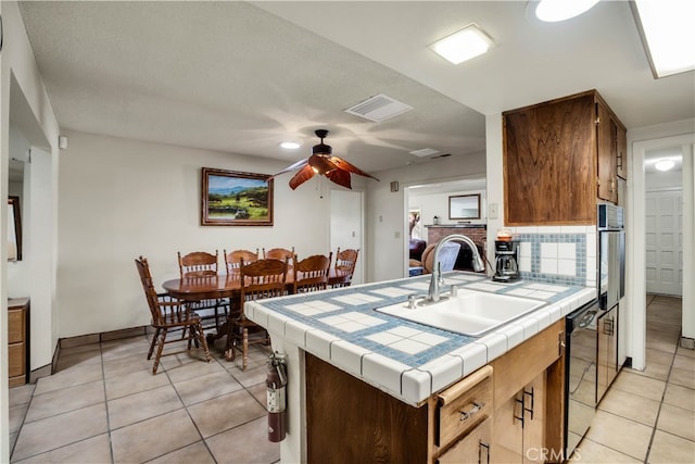 kitchen featuring ceiling fan, light tile patterned floors, sink, tile counters, and black dishwasher