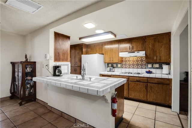 kitchen featuring decorative backsplash, white refrigerator, tile counters, and light tile patterned floors