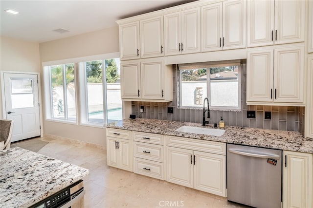 kitchen featuring light stone counters, dishwasher, sink, and a healthy amount of sunlight