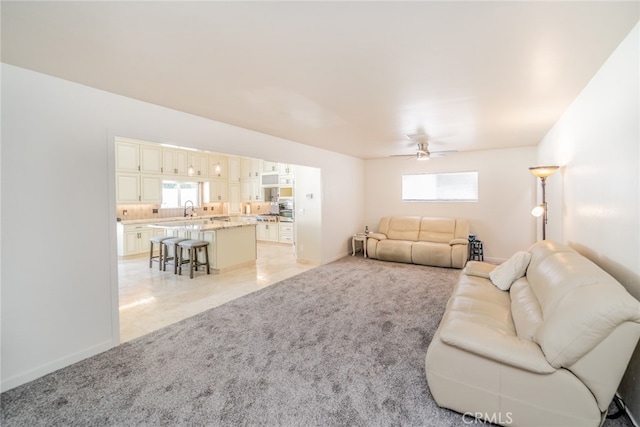 living room featuring ceiling fan, light colored carpet, sink, and a wealth of natural light