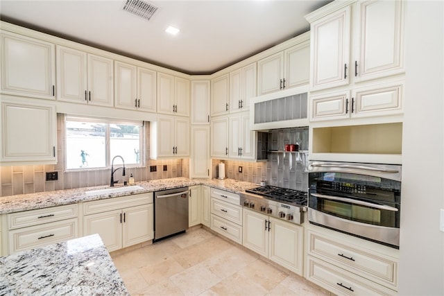 kitchen featuring appliances with stainless steel finishes, backsplash, sink, and light stone counters