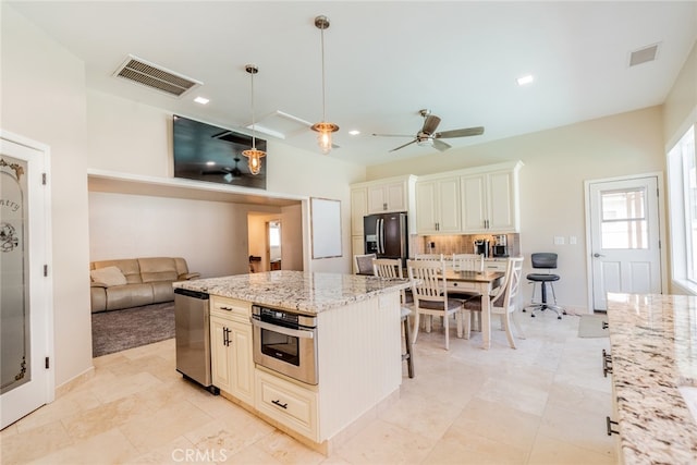 kitchen featuring light stone counters, a center island, a kitchen bar, appliances with stainless steel finishes, and decorative light fixtures