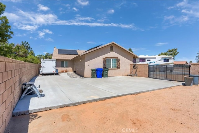 rear view of property with a tile roof, solar panels, stucco siding, a gate, and a fenced backyard