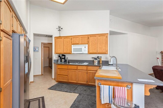 kitchen featuring a breakfast bar, dark tile patterned flooring, sink, stainless steel refrigerator with ice dispenser, and gas stovetop