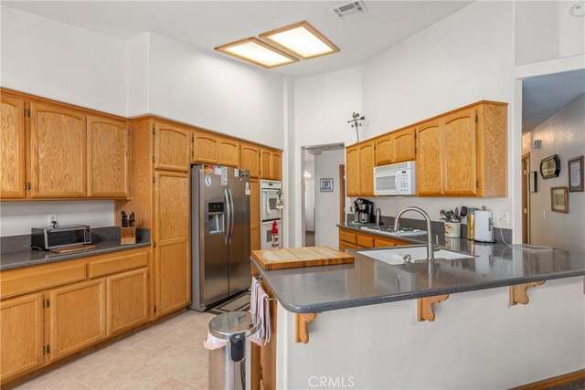 kitchen featuring a high ceiling, white appliances, a kitchen bar, and kitchen peninsula