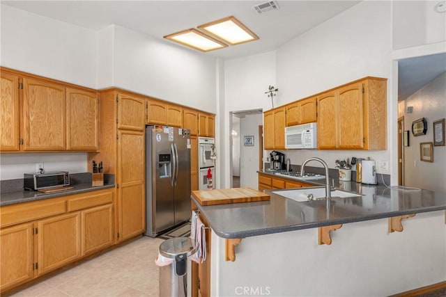 kitchen featuring stainless steel fridge, visible vents, white microwave, a kitchen breakfast bar, and a peninsula