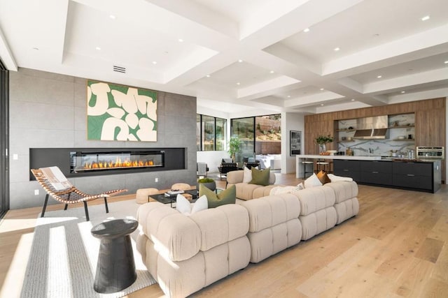 living room with beam ceiling, coffered ceiling, light wood-type flooring, and a fireplace