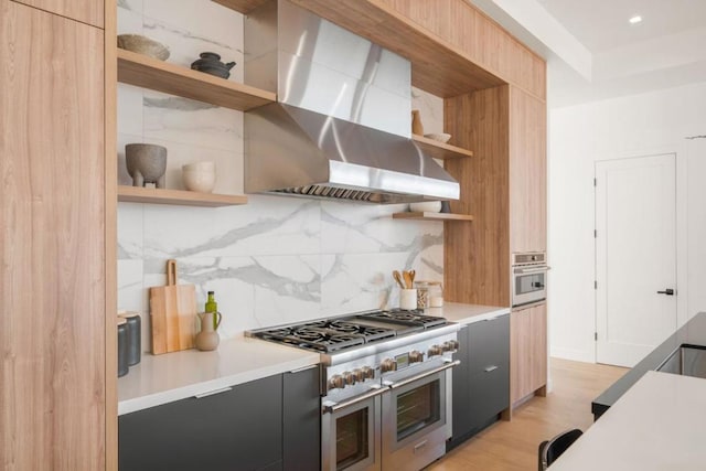 kitchen featuring appliances with stainless steel finishes, wall chimney range hood, backsplash, and light hardwood / wood-style floors