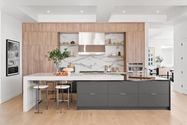 kitchen featuring a spacious island, wall chimney exhaust hood, gray cabinetry, stainless steel appliances, and backsplash