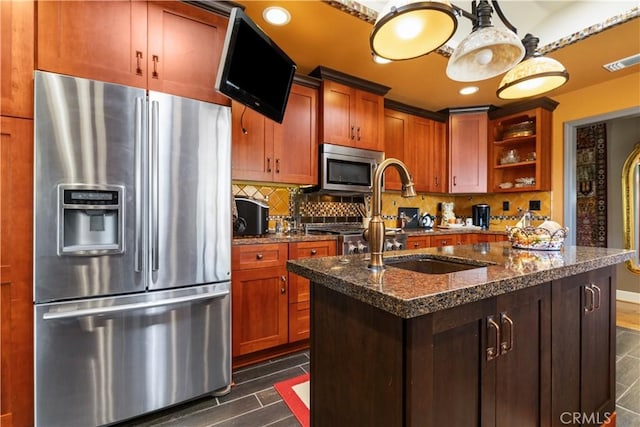 kitchen featuring sink, dark stone countertops, an island with sink, tasteful backsplash, and stainless steel appliances