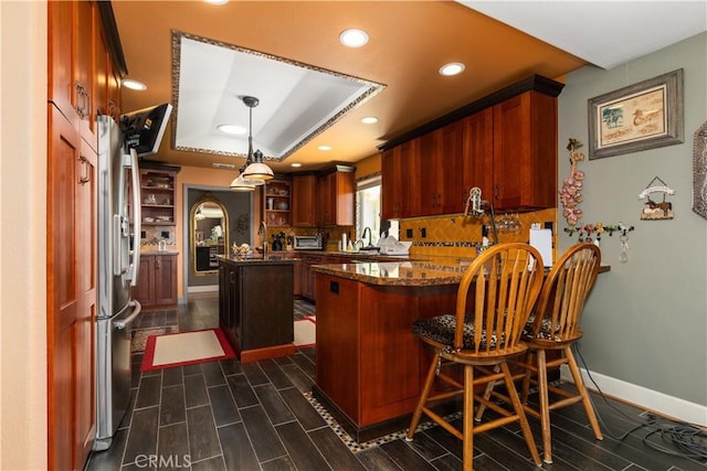 kitchen with kitchen peninsula, stainless steel fridge, dark stone counters, pendant lighting, and a kitchen island