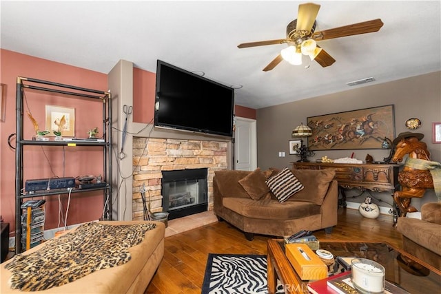 living room featuring hardwood / wood-style floors, a stone fireplace, and ceiling fan