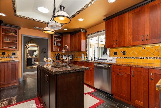 kitchen featuring dishwasher, tasteful backsplash, dark stone countertops, a tray ceiling, and a kitchen island with sink