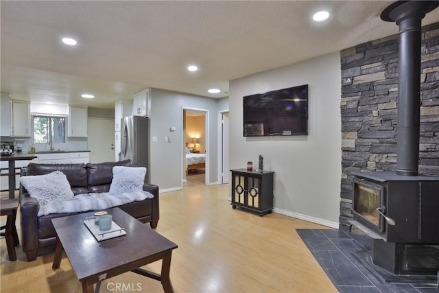 living room featuring light wood-type flooring, a wood stove, and sink