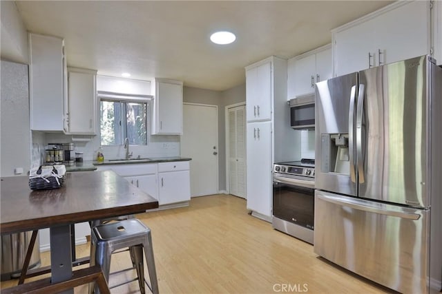 kitchen featuring backsplash, sink, light wood-type flooring, appliances with stainless steel finishes, and white cabinetry