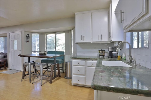 kitchen with white cabinets, tasteful backsplash, sink, and light hardwood / wood-style flooring