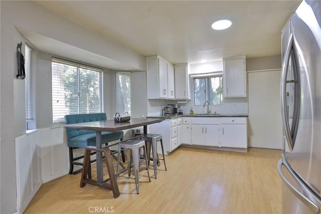 kitchen with stainless steel fridge, sink, white cabinets, and light hardwood / wood-style floors