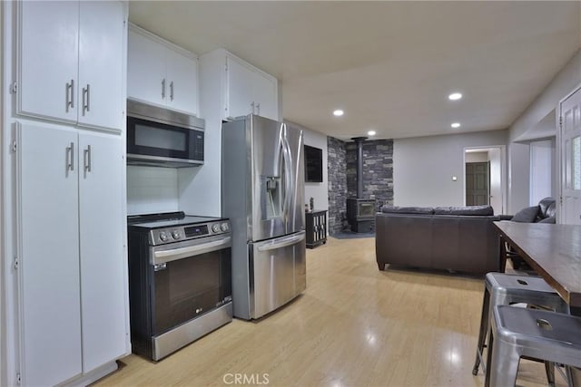 kitchen with white cabinets, a wood stove, stainless steel appliances, and light hardwood / wood-style flooring