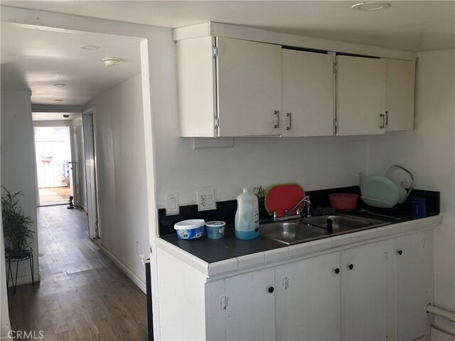 kitchen with tile counters, white cabinetry, hardwood / wood-style flooring, and sink