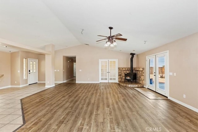 unfurnished living room featuring french doors, lofted ceiling, light hardwood / wood-style flooring, a wood stove, and ceiling fan