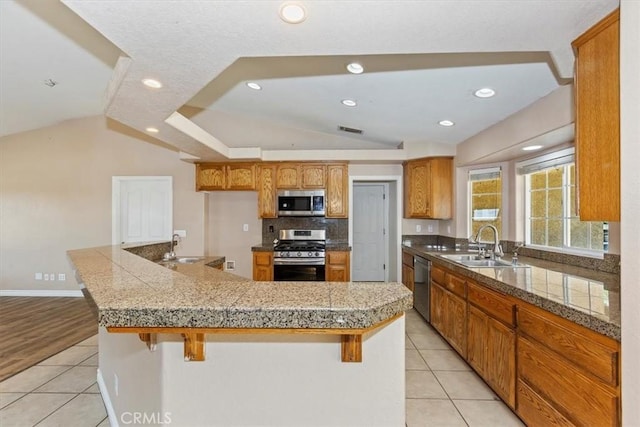 kitchen with light tile patterned floors, stainless steel appliances, lofted ceiling, a breakfast bar, and sink