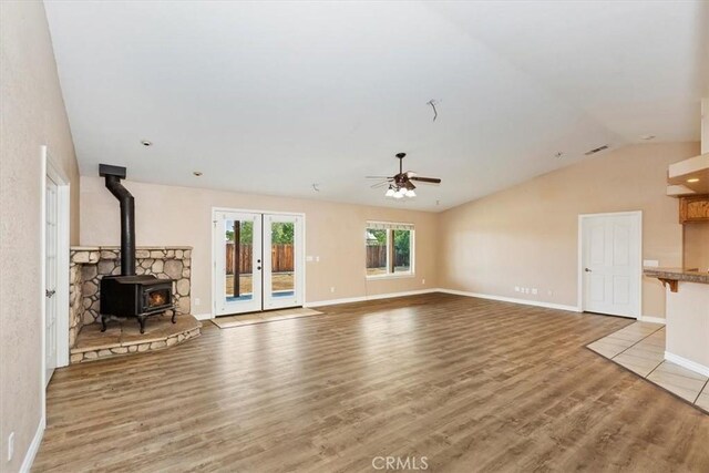 unfurnished living room with ceiling fan, wood-type flooring, a wood stove, and lofted ceiling