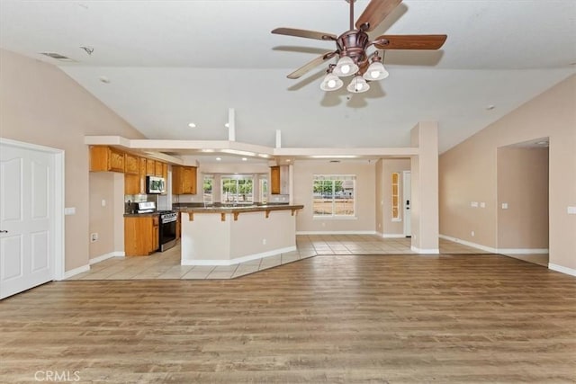 kitchen featuring a breakfast bar area, high vaulted ceiling, appliances with stainless steel finishes, ceiling fan, and light hardwood / wood-style floors