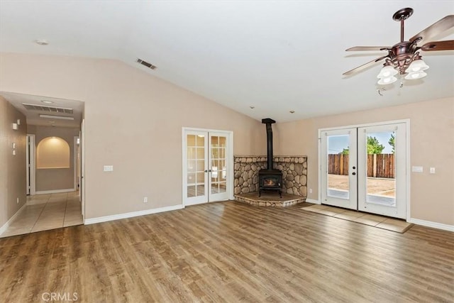 unfurnished living room featuring lofted ceiling, a wood stove, hardwood / wood-style flooring, ceiling fan, and french doors