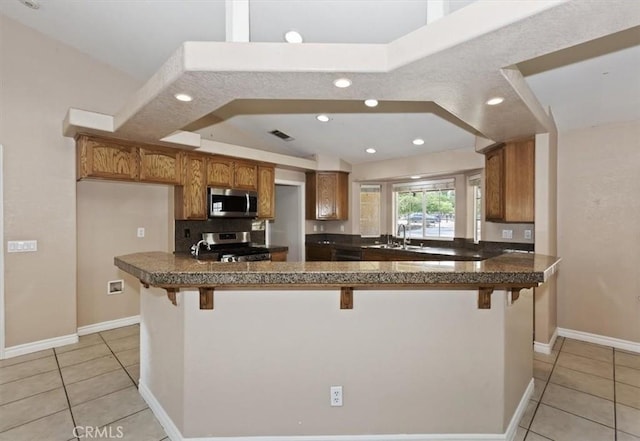 kitchen featuring stainless steel appliances, a kitchen bar, kitchen peninsula, and sink