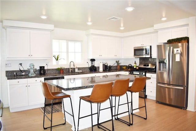 kitchen featuring white cabinetry, sink, appliances with stainless steel finishes, a kitchen island, and light wood-type flooring