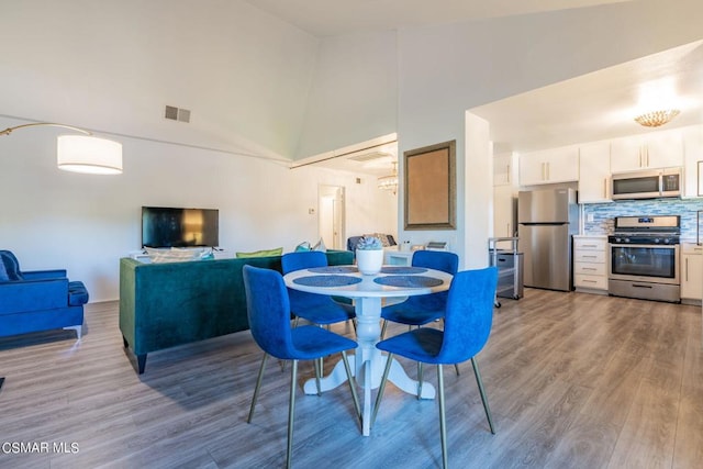 dining area with high vaulted ceiling and light wood-type flooring