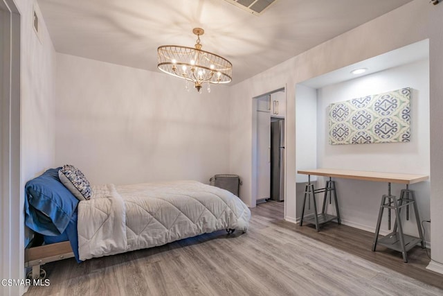 bedroom with stainless steel fridge, an inviting chandelier, and hardwood / wood-style floors