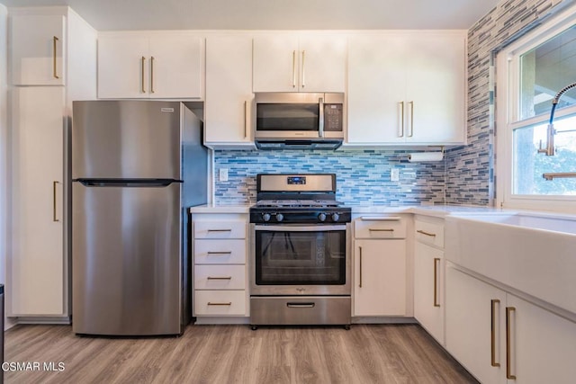 kitchen featuring appliances with stainless steel finishes, white cabinetry, light hardwood / wood-style floors, sink, and backsplash