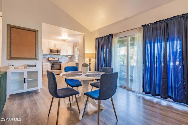 dining room with high vaulted ceiling and light hardwood / wood-style flooring