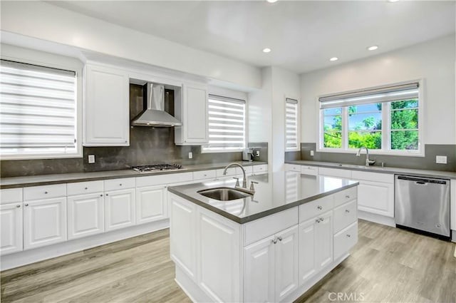 kitchen with a kitchen island with sink, wall chimney range hood, sink, white cabinetry, and stainless steel appliances